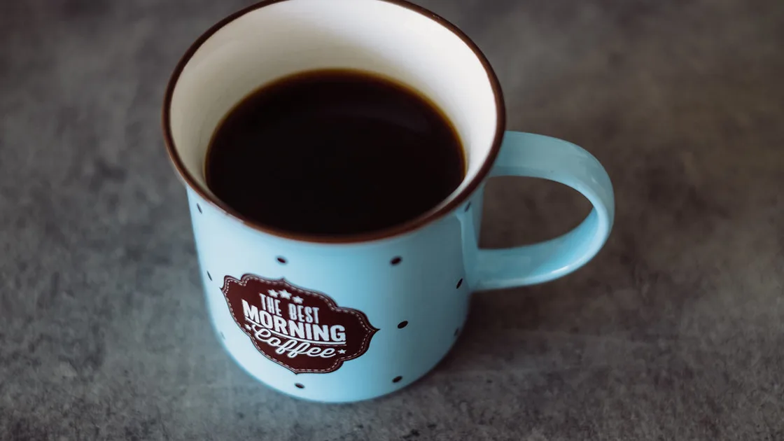 A pale blue enamel mug of black coffee resting on a grey stone surface. BMI Tracker - bmi-tracker.com