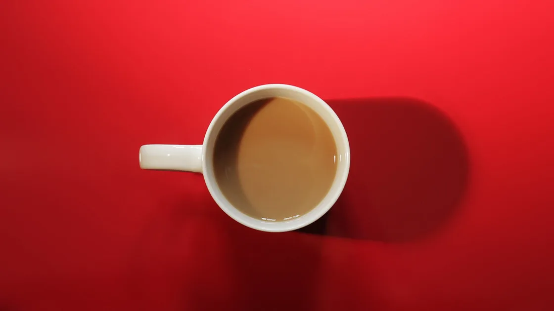 A single white cup of coffee photographed from above on a bright red background. BMI Tracker - bmi-tracker.com